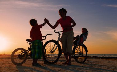 Gün batımında, Bisiklet üzerinde iki çocuklu anne motorcu aile siluet