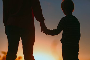 Gün batımında el ele tutuşan baba ve oğulun silueti.
