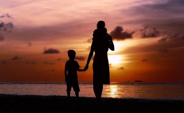 Mor och två barn gå på stranden vid solnedgången — Stockfoto