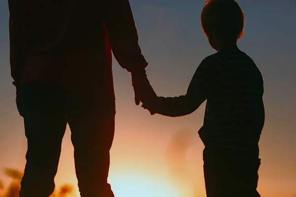Silhuett av far och son som håller hand vid solnedgången — Stockfoto