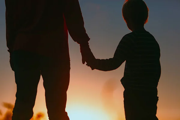 Silhueta de pai e filho de mãos dadas ao pôr do sol — Fotografia de Stock