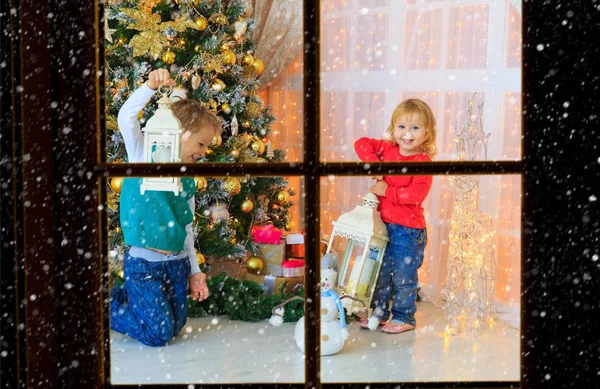 Μικρό αγόρι και κορίτσι διακόσμηση του Χριστουγεννιάτικου δέντρου, θέα από το εξωτερικό παράθυρο — Φωτογραφία Αρχείου
