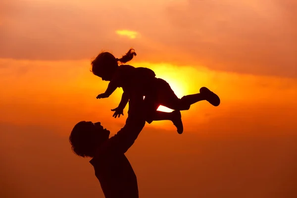 Pai e pequena filha silhuetas jogar ao pôr do sol — Fotografia de Stock
