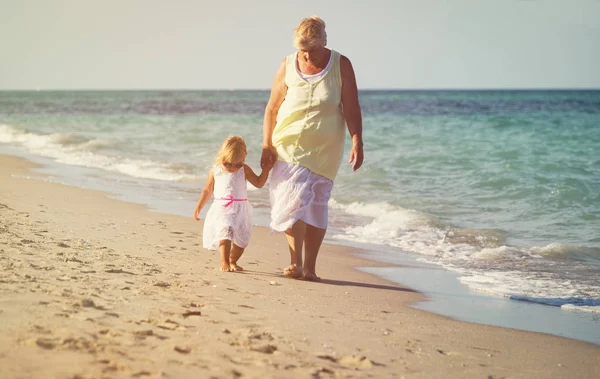 Glückliche Großmutter mit kleinem Mädchen spazieren am Strand — Stockfoto