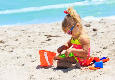 Tatlı küçük kız kumsalda kumla oynuyor.