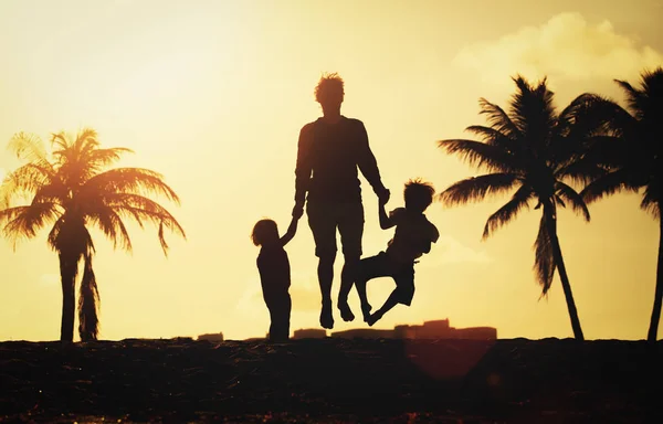Gelukkig gezin op strand - vader met kinderen springen van vreugde bij zonsondergang — Stockfoto