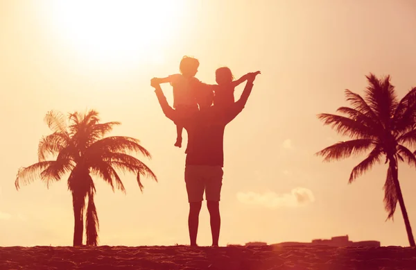 Silueta del padre con dos niños juegan en la playa puesta del sol — Foto de Stock