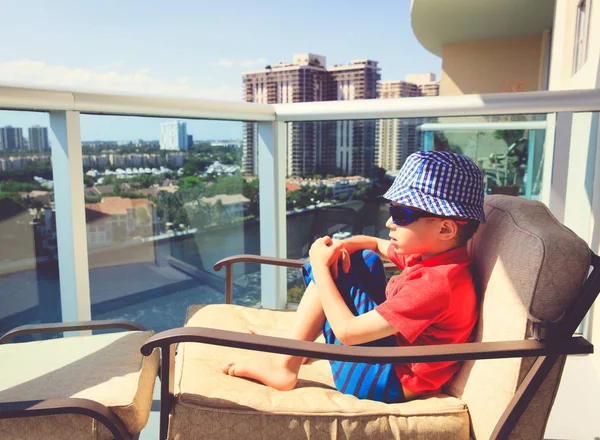 Liten pojke koppla av i hotel tittar på stadsbilden med balkong — Stockfoto