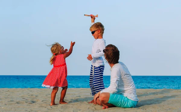 Vader met twee kinderen spelen speelgoed vliegtuig op strand, familie reizen — Stockfoto