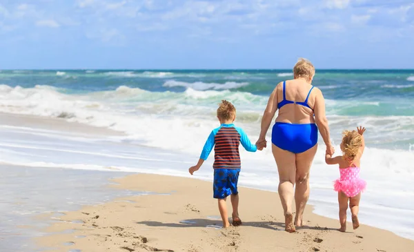 Šťastná babička s dětmi - malý chlapec a dívka go plavání na pláži — Stock fotografie