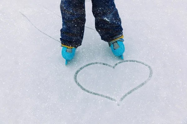 Liefde schaatsen concept - voeten van het kind in het schaatsen en hart op sneeuw — Stockfoto