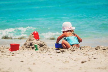 Tatlı küçük kız kumsalda kumla oynuyor.