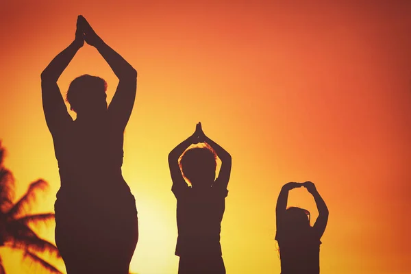 family silhouettes doing yoga at sunset beach