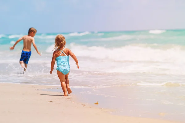 Fetiță și băiat alerga juca cu valuri pe plajă — Fotografie, imagine de stoc