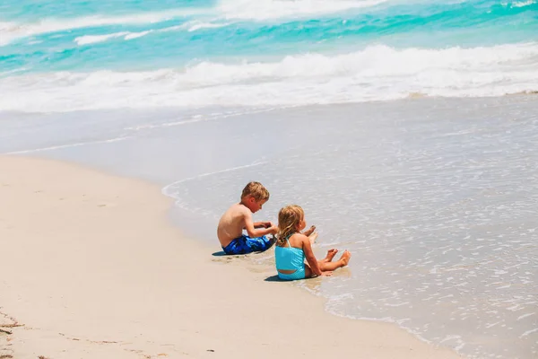 Ittle menino e menina jogar com água na praia — Fotografia de Stock