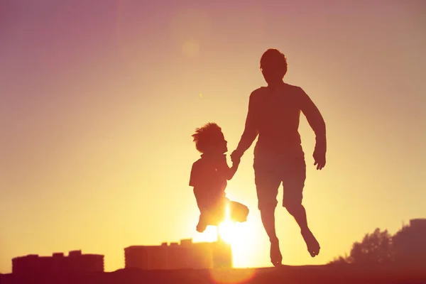 Pai e filho pulando na praia do pôr do sol — Fotografia de Stock