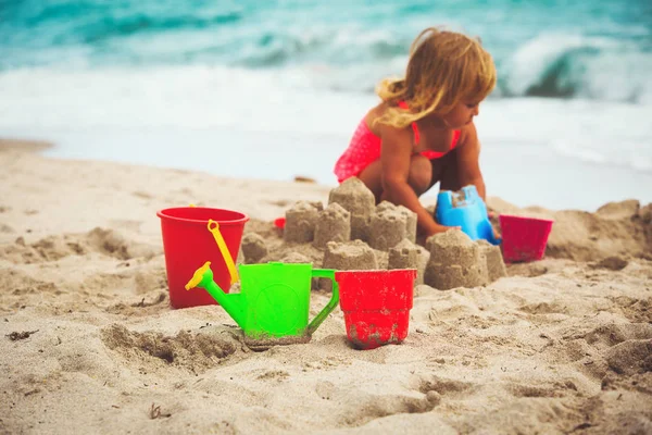Дитячі іграшки та маленька дівчинка будують пісочний замок — стокове фото