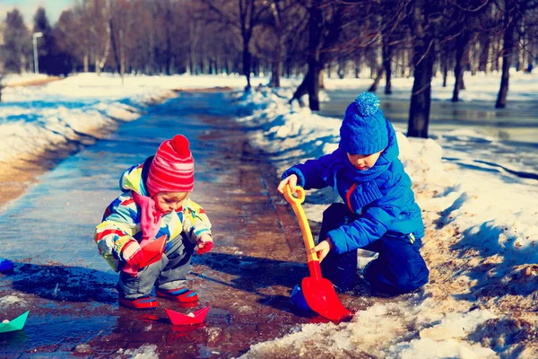 Little boy and girl plaing with paper boats in spring puddle — Stock Photo, Image