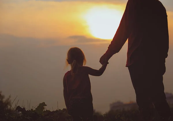 Silhueta de pai e filha de mãos dadas ao pôr do sol — Fotografia de Stock