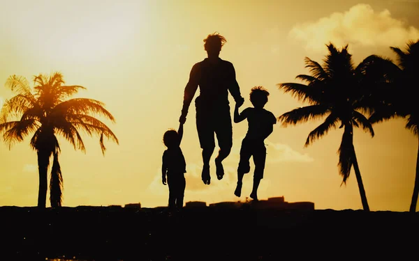 Батько з маленьким сином і дочкою стрибає на пляжі заходу сонця — стокове фото