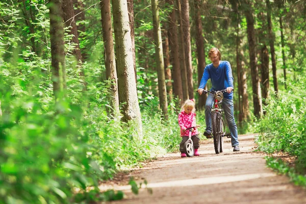 family sport - father and daughter riding bikes in green forest
