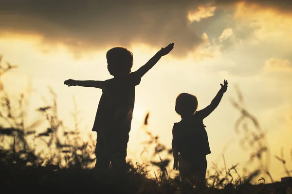 Silhuetas menino e menina jogar ao pôr do sol — Fotografia de Stock