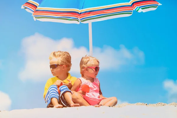 Pequeno menino e menina local sob guarda-sol na praia de verão — Fotografia de Stock