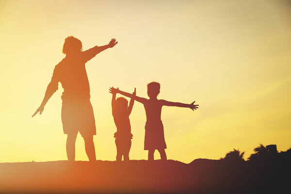 father with son and daughter silhouettes play at sunset