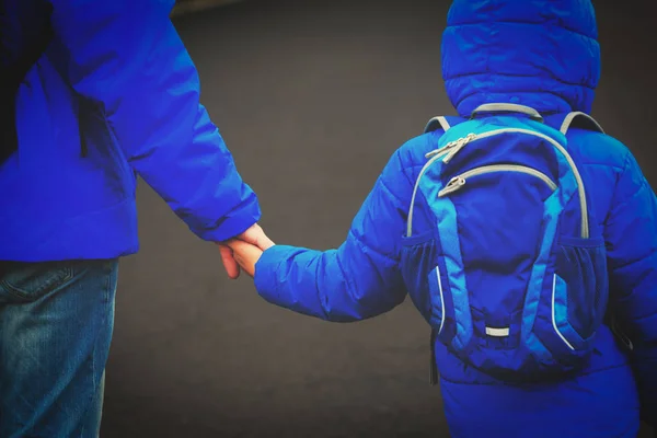 Отец держит сына за руку с рюкзаком на дороге — стоковое фото