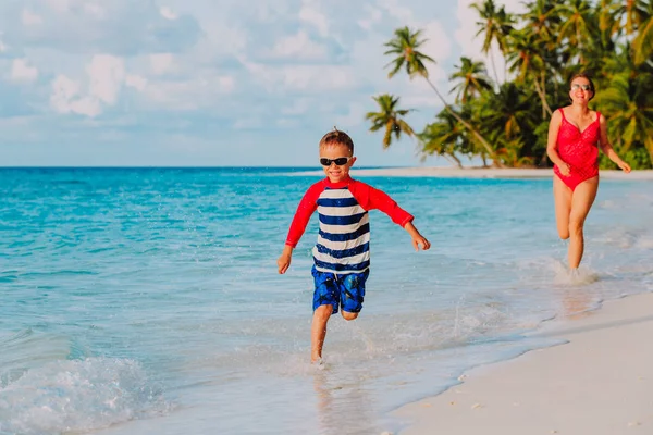 Mãe feliz e filho correndo na água na praia — Fotografia de Stock