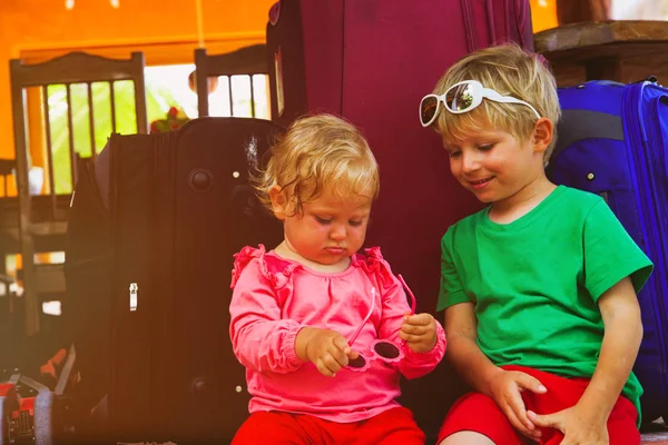 Kleiner Junge und kleines Mädchen sitzen auf reisebereiten Koffern — Stockfoto