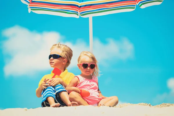 Ładny mały chłopiec i dziewczyna grać na plaży pod parasol — Zdjęcie stockowe