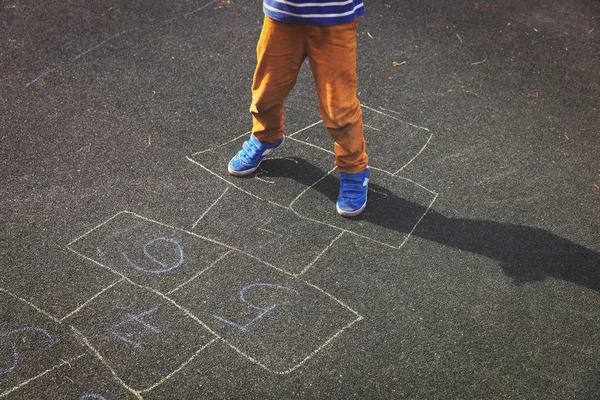 เด็กน้อยเล่นฮ็อปสก็อตช์บนสนามเด็กเล่น — ภาพถ่ายสต็อก