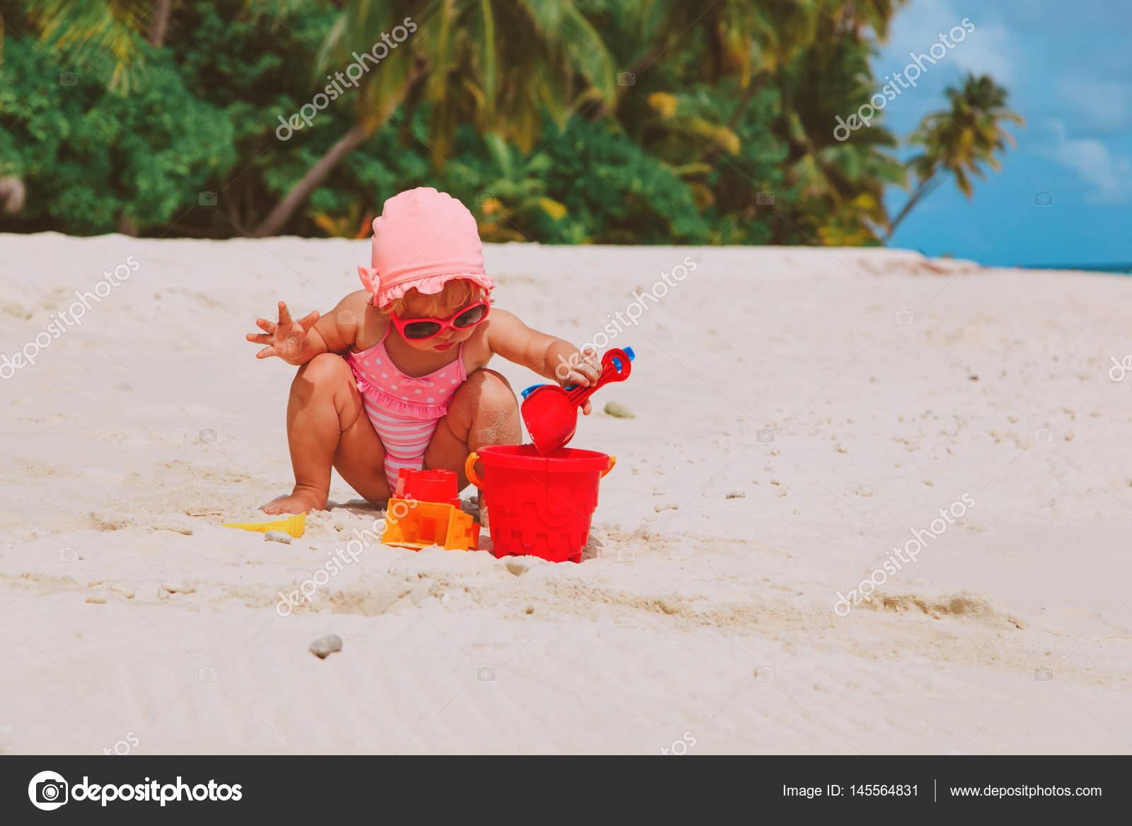 Criança sentada e escrevendo com o dedo na praia de areia 