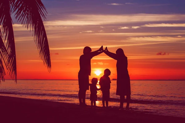 Cuidados familiares - pais felizes fazendo casa para as crianças ao pôr do sol — Fotografia de Stock