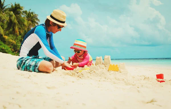 Padre e hija pequeña juegan con arena en la playa — Foto de Stock