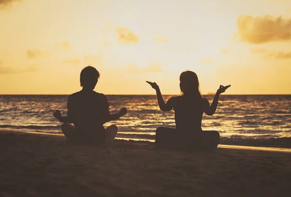 Silhueta de casal fazendo ioga ao pôr do sol — Fotografia de Stock