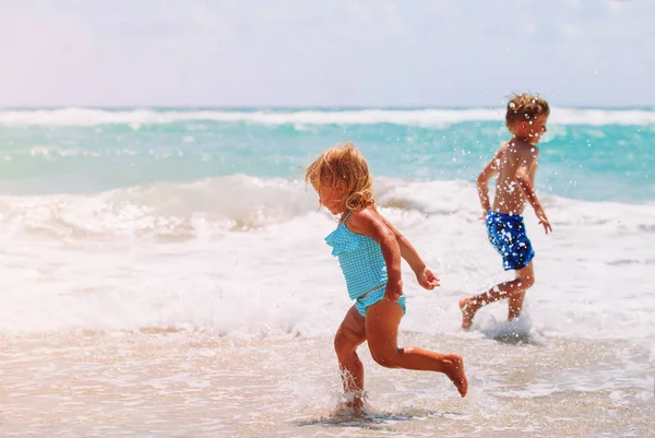 Klein meisje en jongen lopen spelen met golven op het strand — Stockfoto