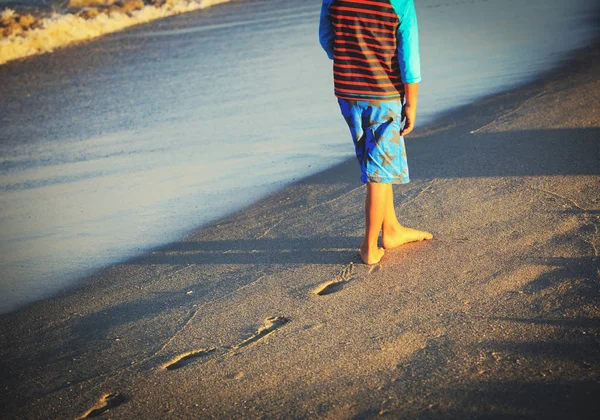 Мальчик ходит по пляжу оставляя следы на песке — стоковое фото