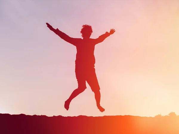 Silhueta de jovem feliz pulando ao pôr do sol — Fotografia de Stock