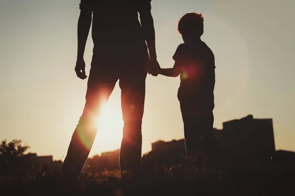 Silhueta de pai e filho de mãos dadas ao pôr do sol — Fotografia de Stock