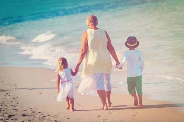 Oma met kinderen - kleine jongen en meisje lopen op strand — Stockfoto