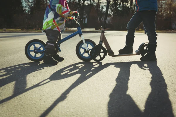 Niños montar en bicicleta y scooter al atardecer — Foto de Stock