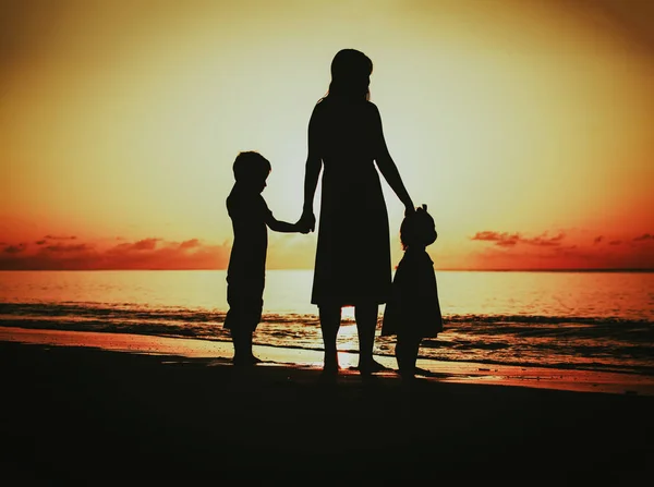 Moeder en twee kinderen lopen op het strand bij zonsondergang — Stockfoto