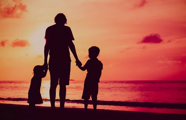 Pai e duas crianças andando na praia ao pôr do sol — Fotografia de Stock