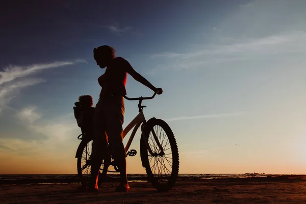 Silhueta de mãe e bebê de bicicleta ao pôr do sol — Fotografia de Stock