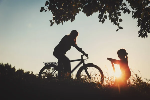 Mother and little daughter riding bike and scooter at sunset — Stock Photo, Image