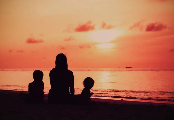 Mor och två barn titta på solnedgången på stranden — Stockfoto