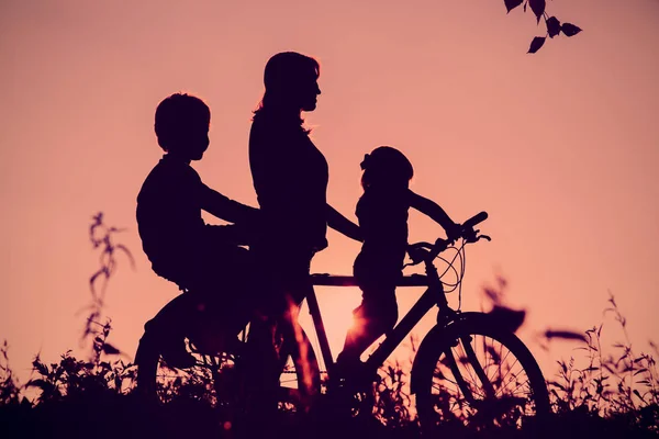 Mãe com filho e filha andar de bicicleta ao pôr do sol — Fotografia de Stock