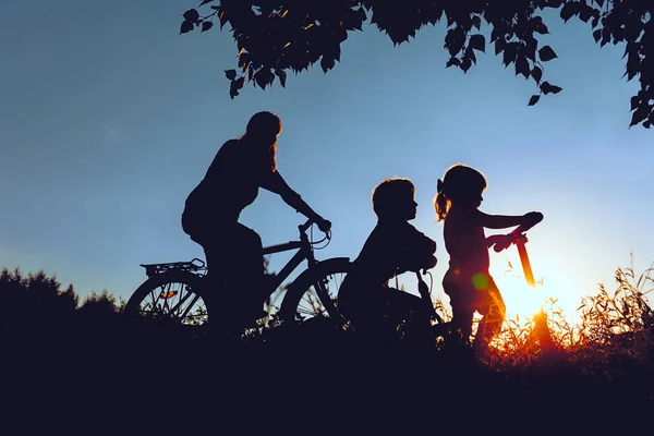 Moeder met zoon en dochter paardrijden fietsen en scooter bij zonsondergang — Stockfoto